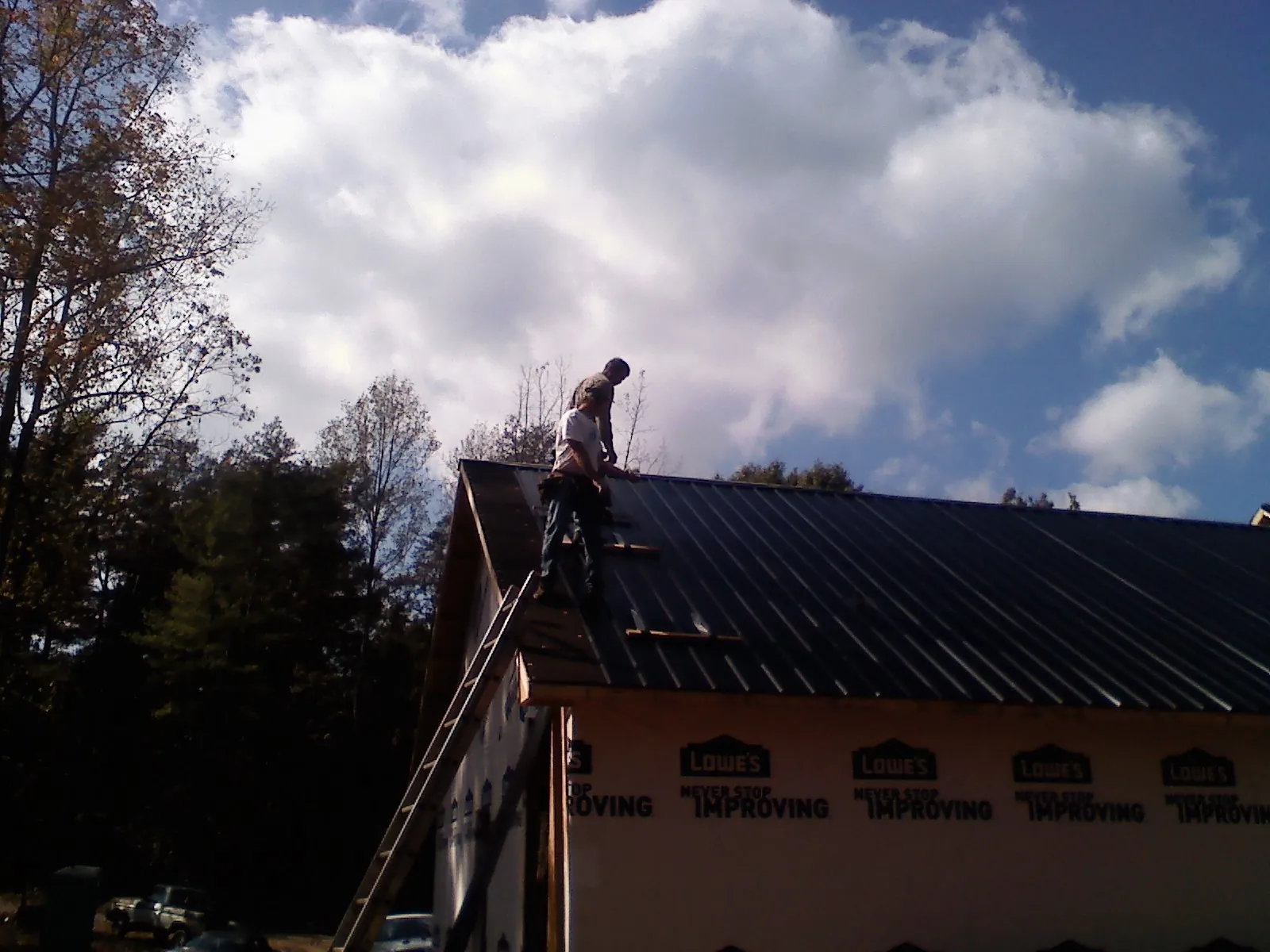Roofer fastening dark metal panels high against a cloudy sky, from a Roof Inspection job in Mc Intosh