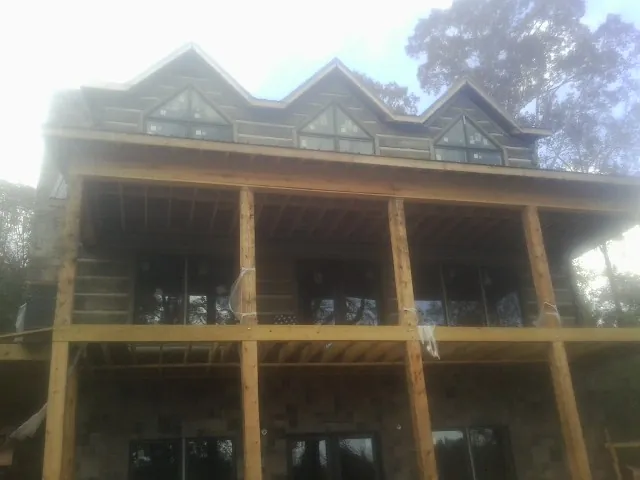 Dormers and porch framing on a large log home under construction — Roof Coating work by our crew in Mc Intosh